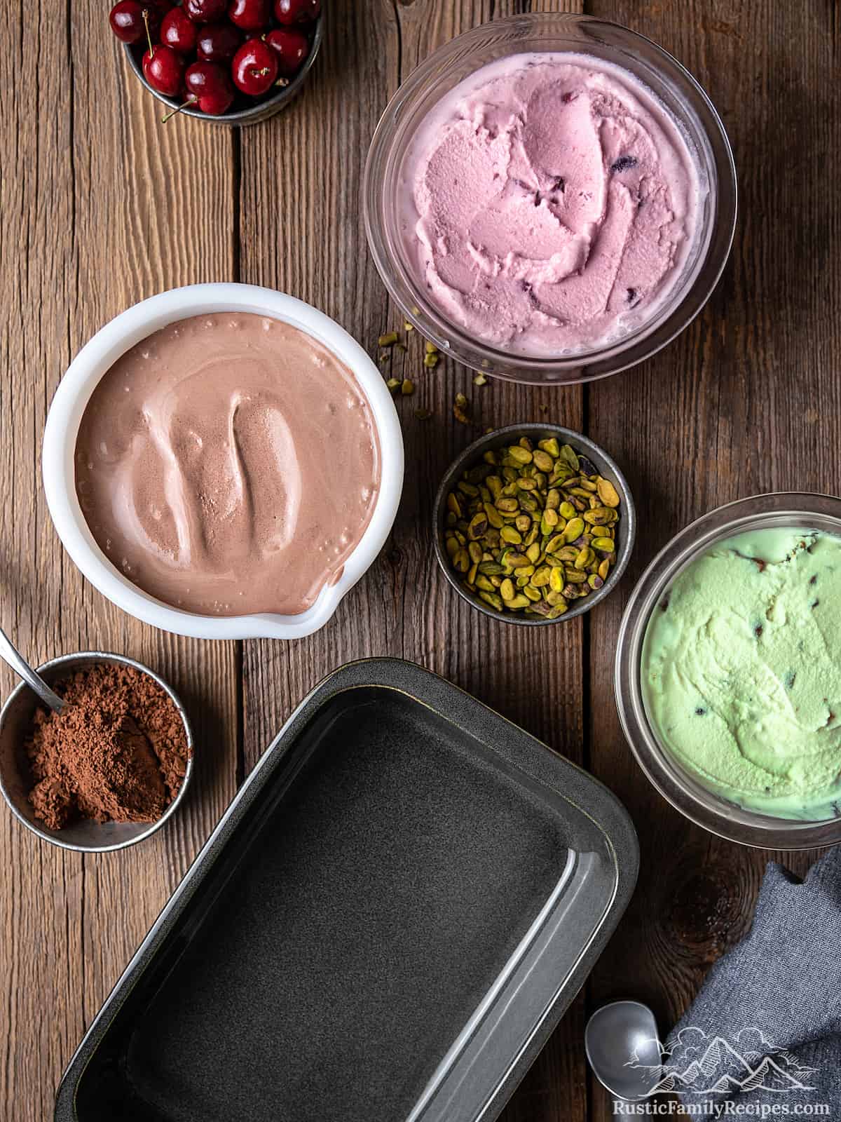 Bowls of chocolate ice cream, cherry ice cream, and pistachio ice cream next to their add-ins, and an empty pan.