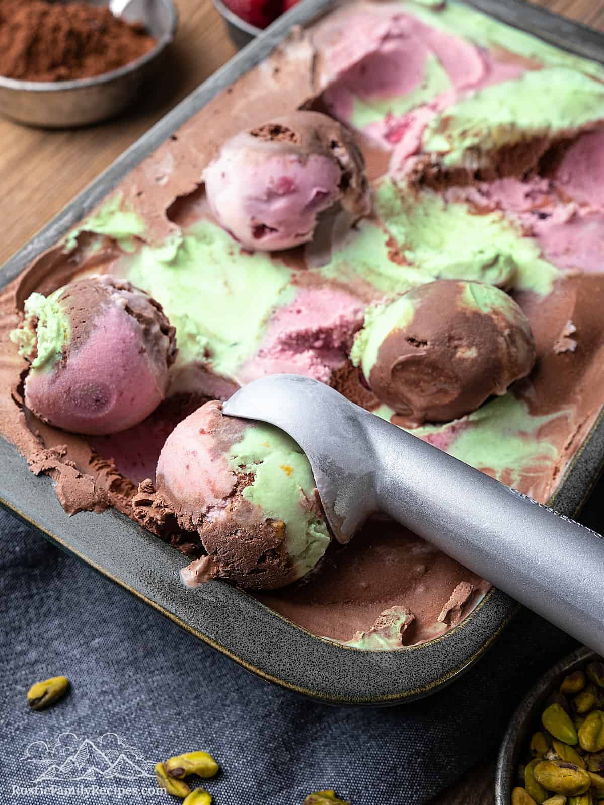 An ice cream scoop scoops a ball of spumoni ice cream from a pan.