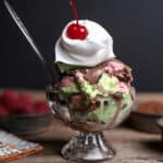 Spumoni ice cream in a glass bowl topped with whipped cream and a cherry.