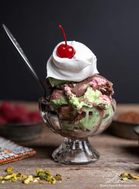 Spumoni ice cream in a glass bowl topped with whipped cream and a cherry.
