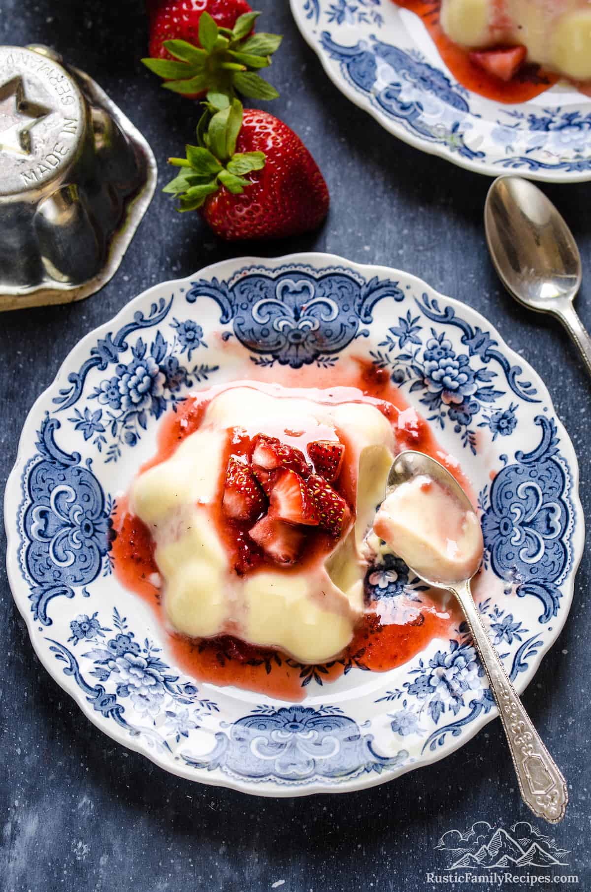 Top view of vanilla budino topped with strawberry sauce on a plate, with spoonfuls missing.