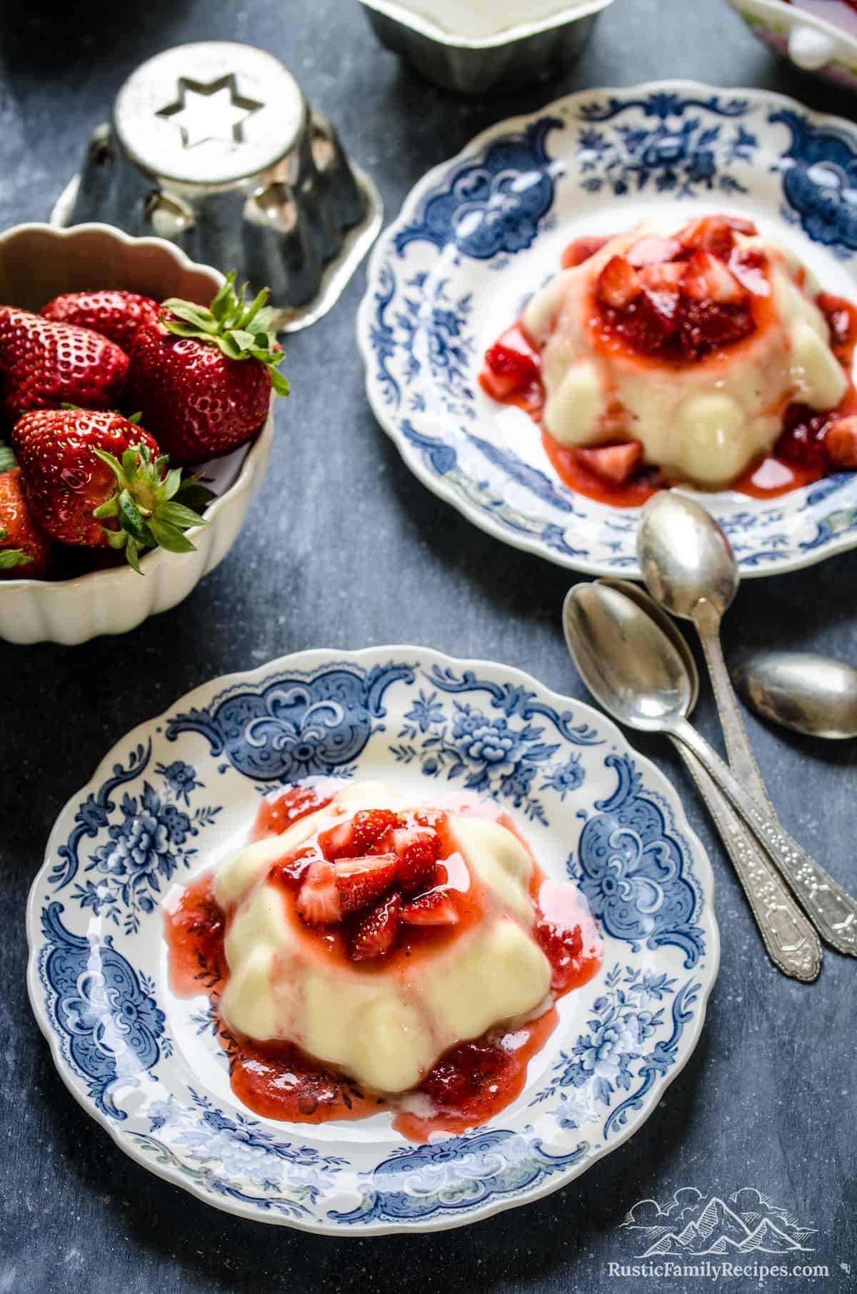 Top view of two vanilla budinos topped with strawberry sauce on Delftware plates.