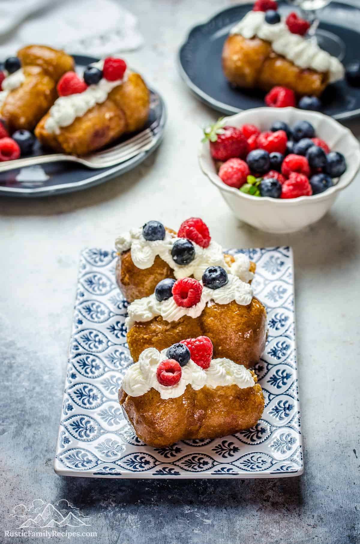 3 rum babas on a plate with whipped cream and berries