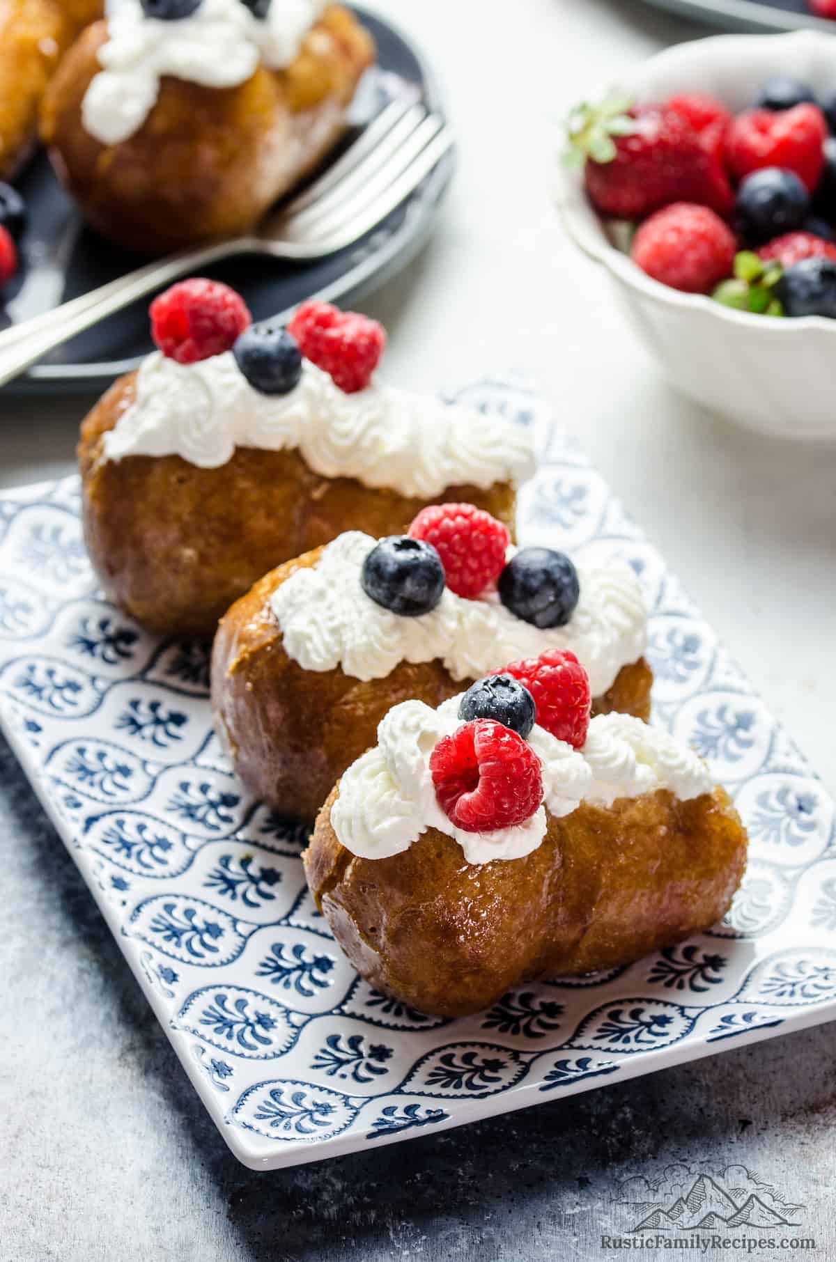 3 rum babas on a plate with whipped cream and berries