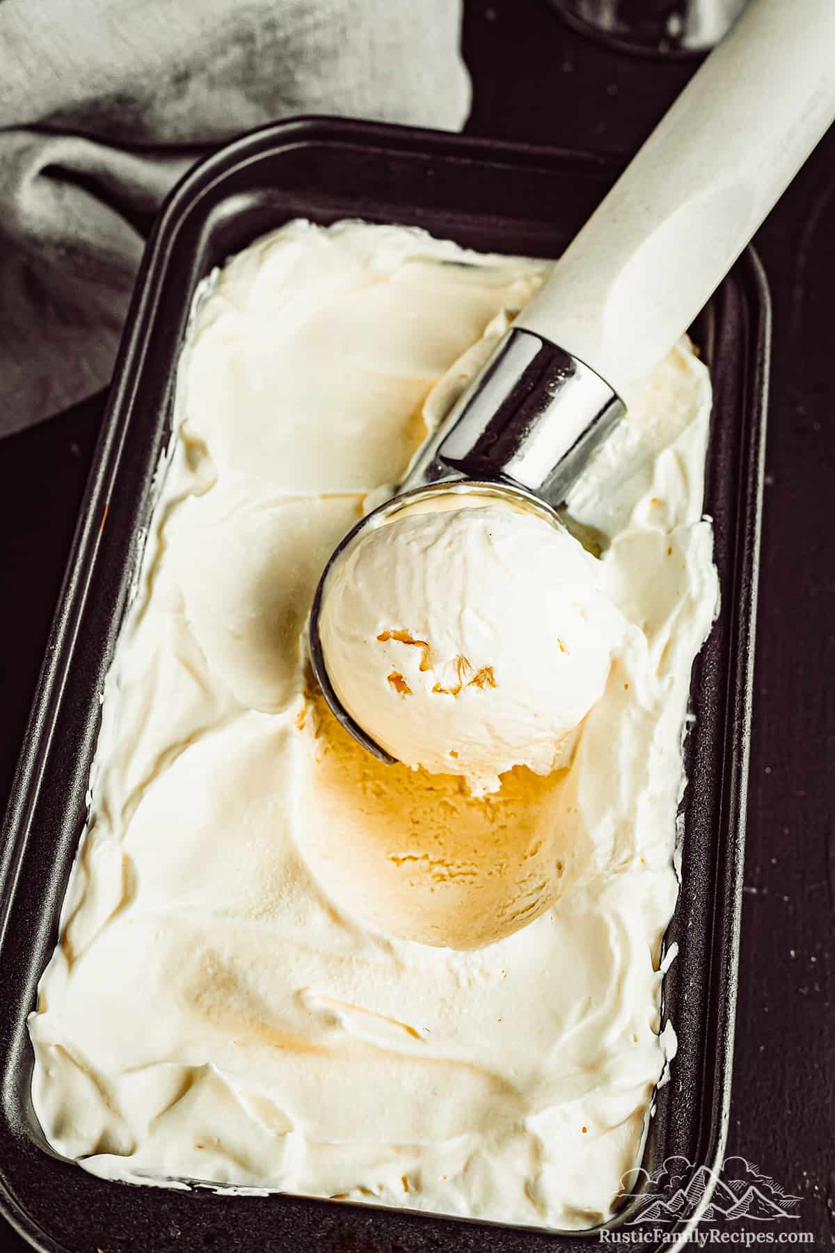 An ice cream scoop scoops an ice cream ball from a loaf pan filled with homemade bourbon vanilla ice cream.