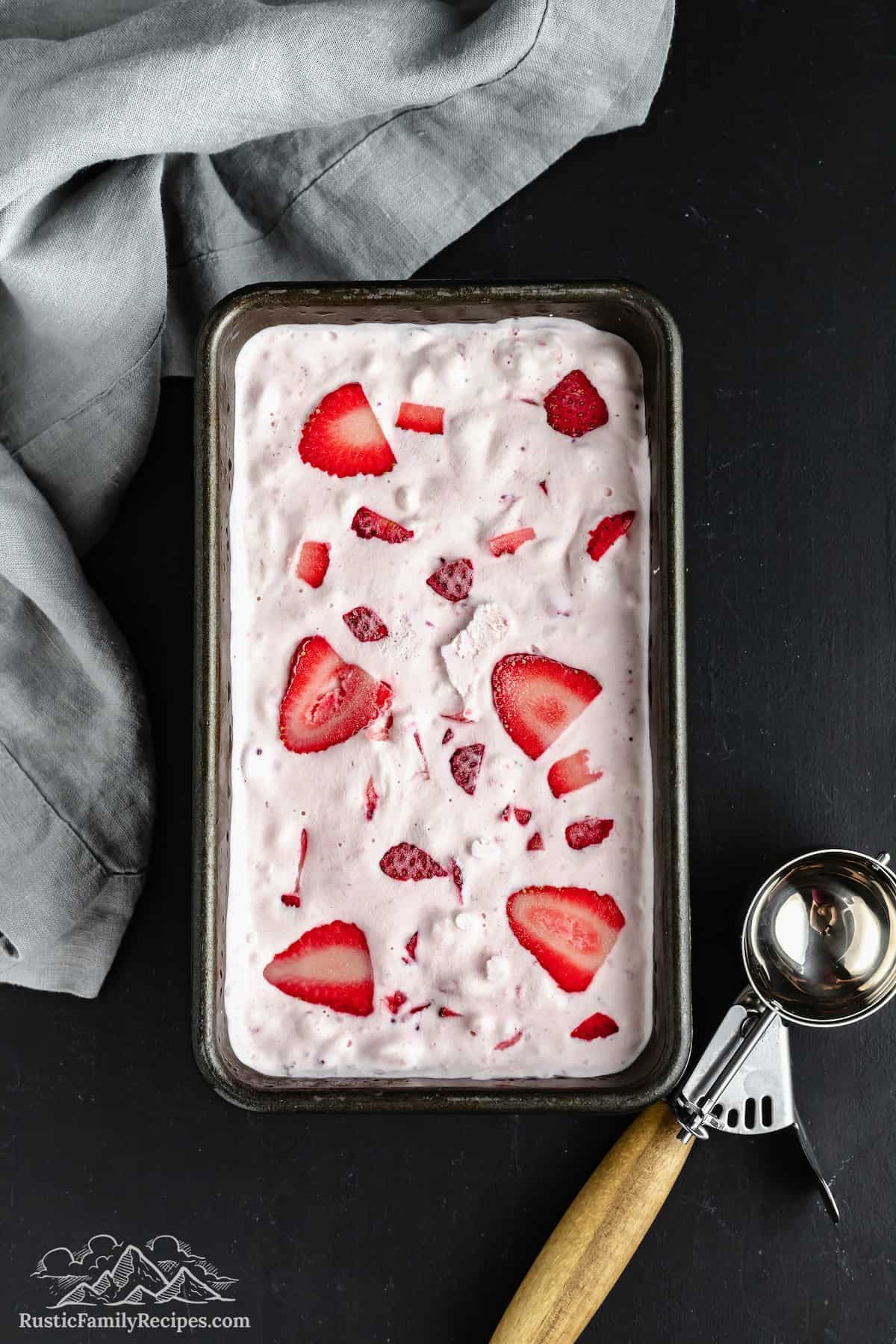 Top view of a pan filled with homemade strawberry ice cream, next to an ice cream scoop.