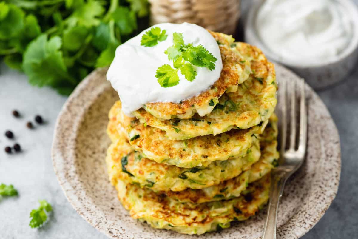 A stack of zucchini corn griddle cakes on a plate with sour cream