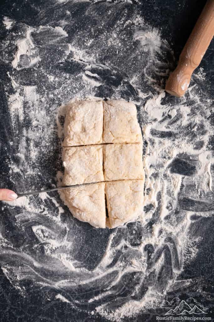 A hand uses a knife to cut a rectangle of shortcake biscuit dough into 6 equal parts.