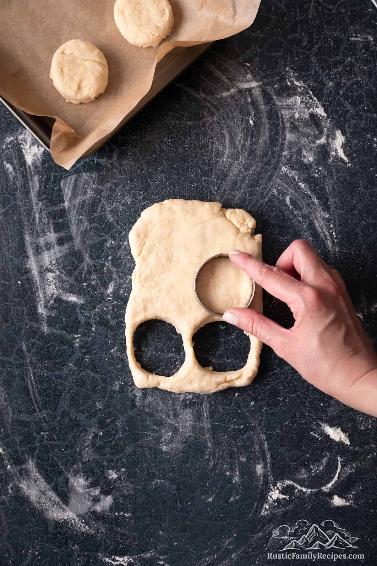 A hand used a cookie cutter to cut circular biscuits from the dough.