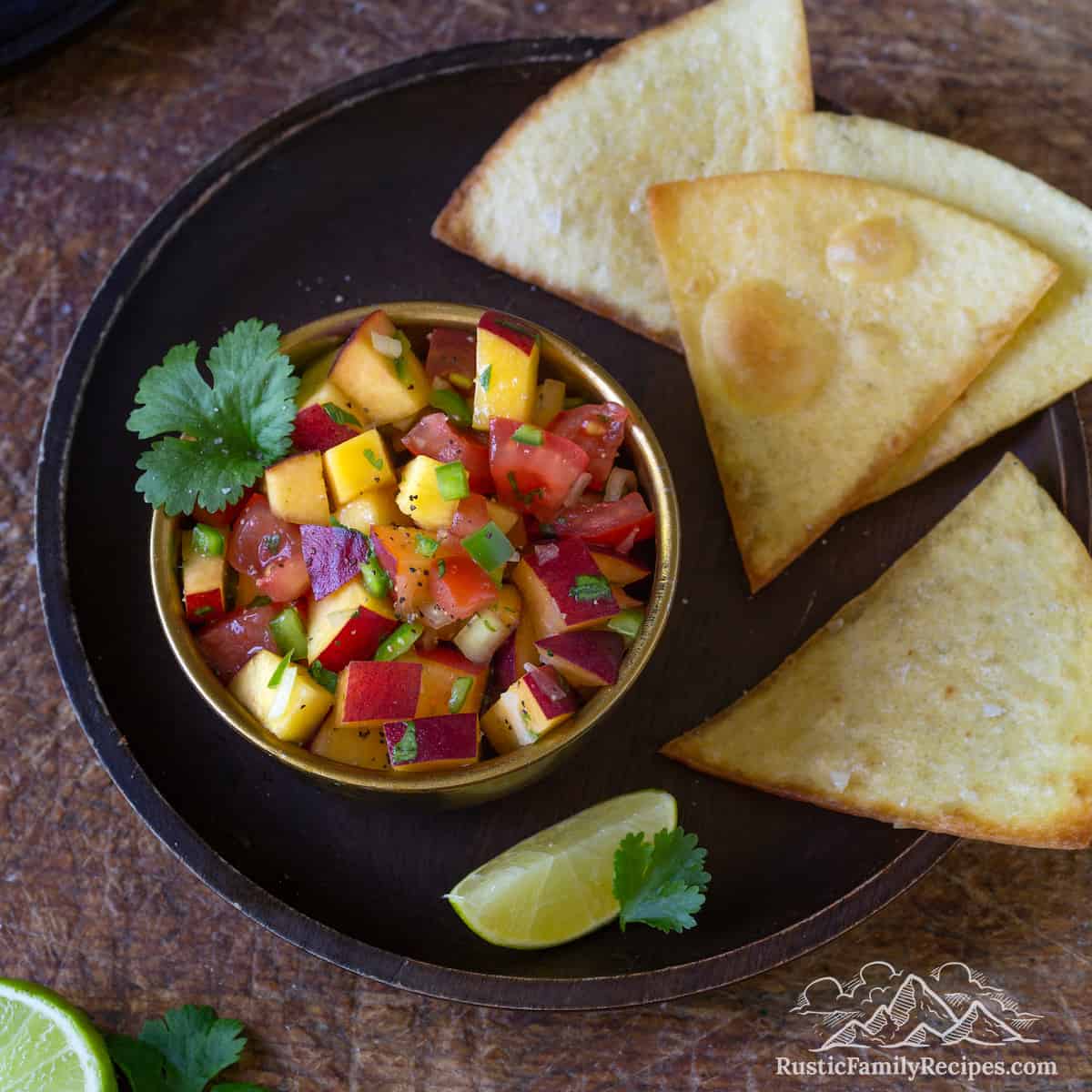 A bowl of peach salsa with totopos on a plate