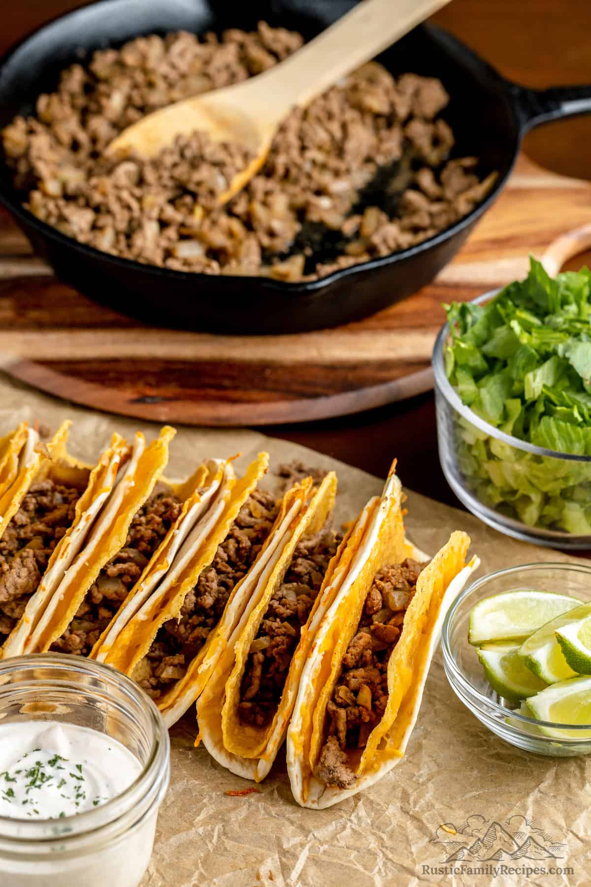 Double-layered taco shells in a row in front of a skillet, filled with taco meat.