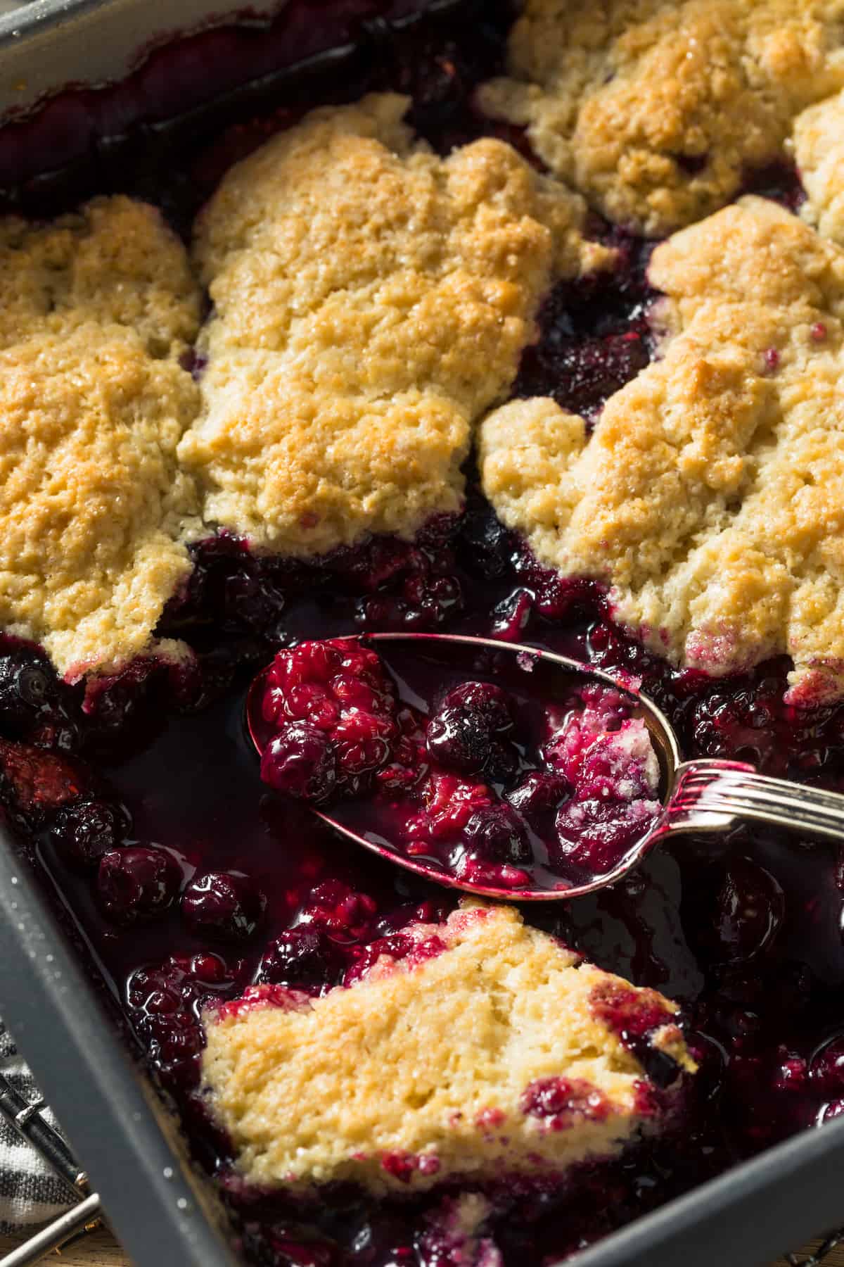 Close up of a jumbleberry cobbler with a scoop taken out, spoon in the pan