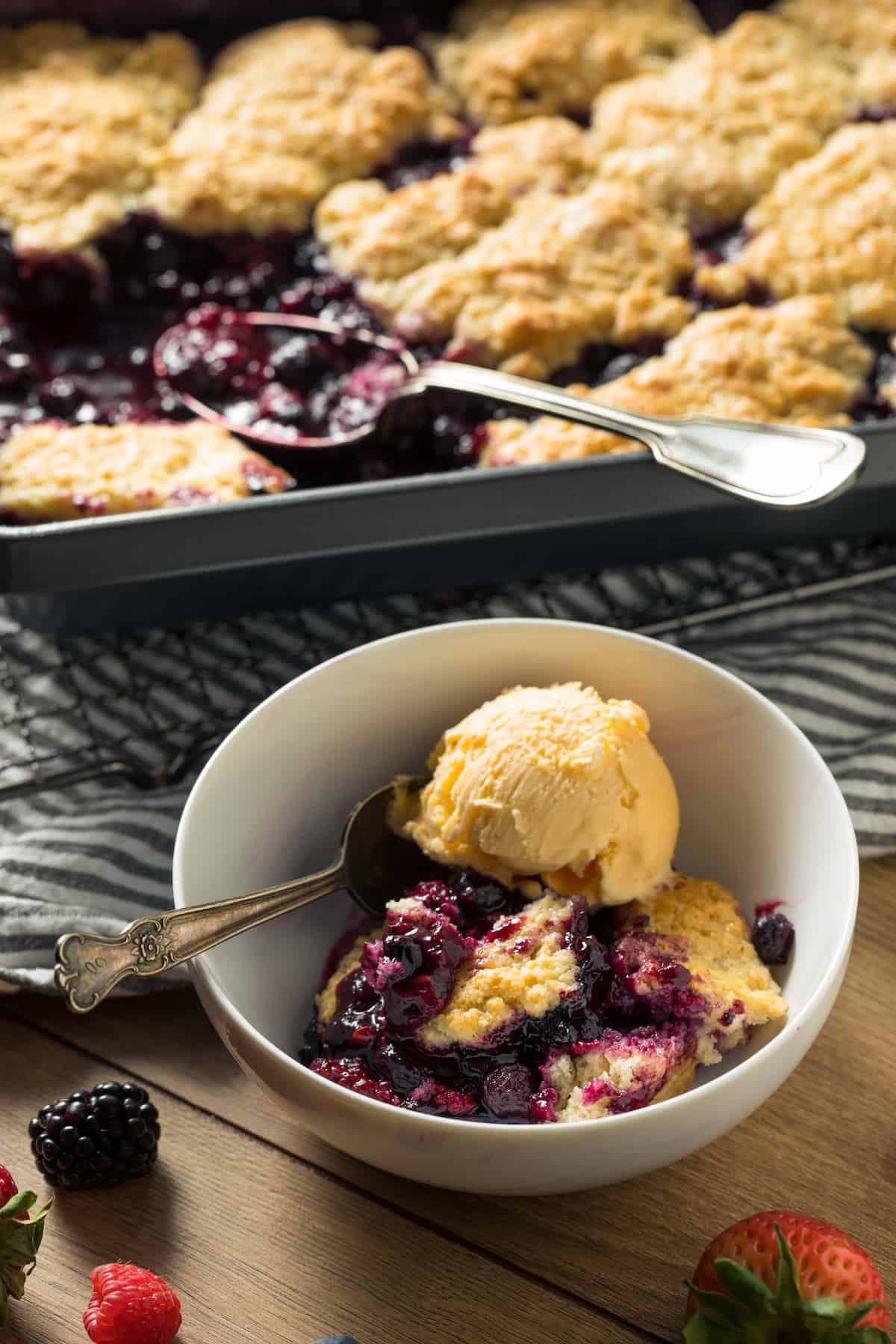 Mixed berry cobbler in a pan, with a serving in a bowl with ice cream