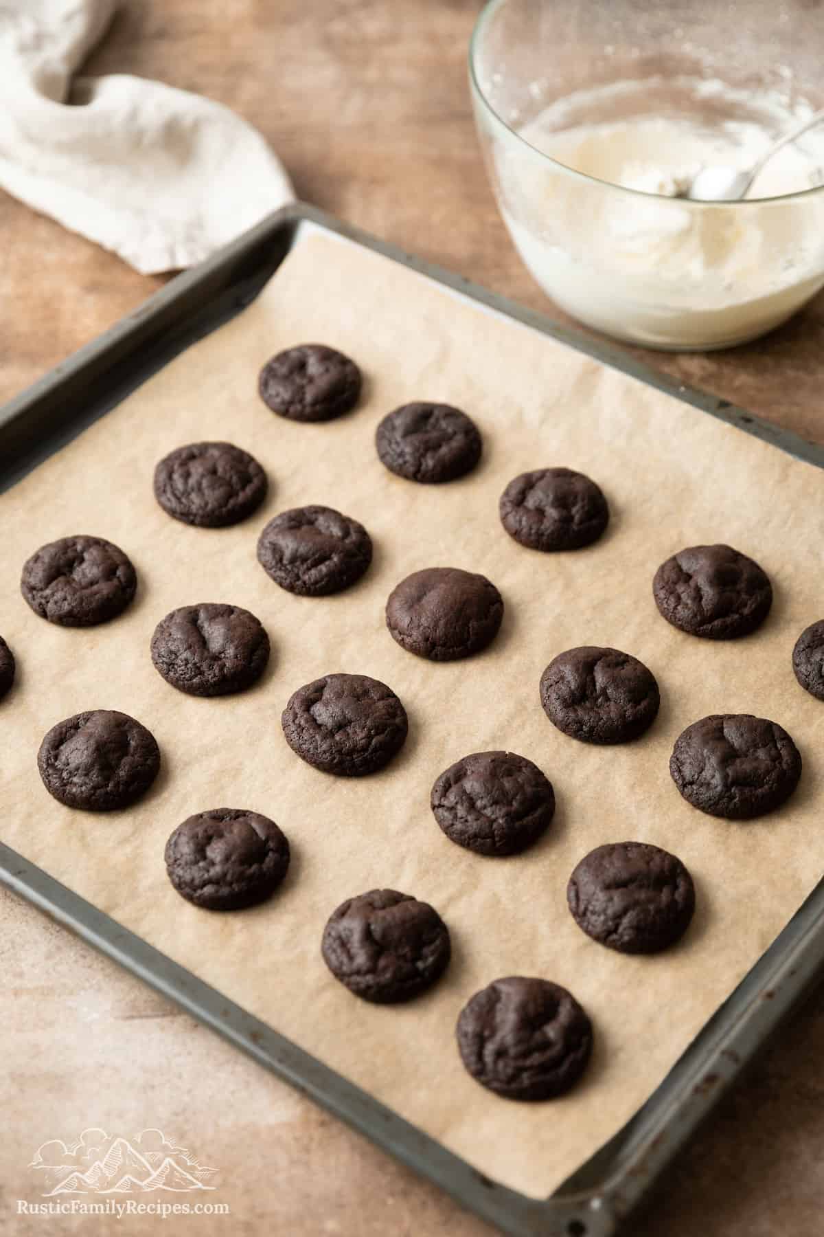 Baked chocolate cookies in rows on a parchment-lined baking sheet.