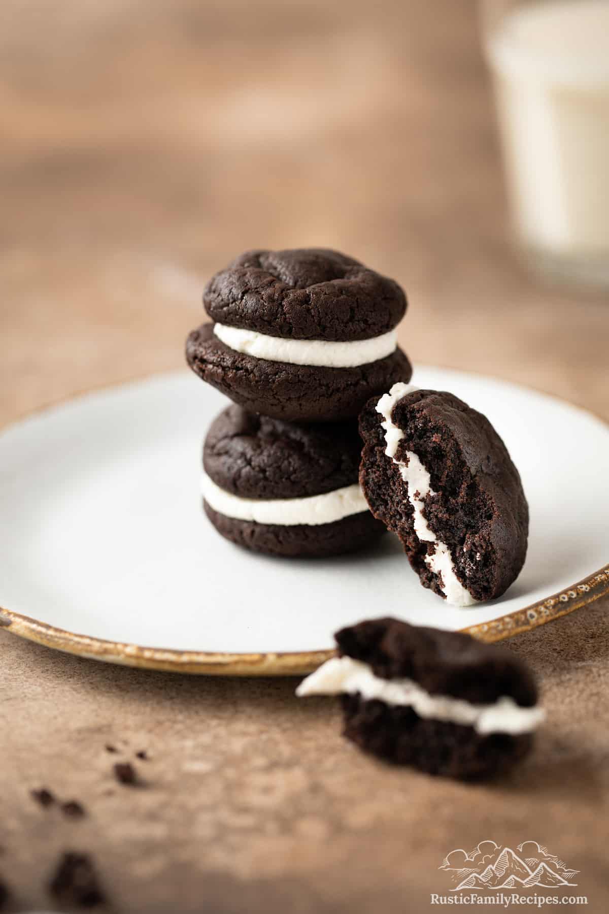 Two Oreo whoopie pies stacked on a white plate, with a third whoopie pie cut in half to reveal the chocolate cookie and vanilla filling layers.