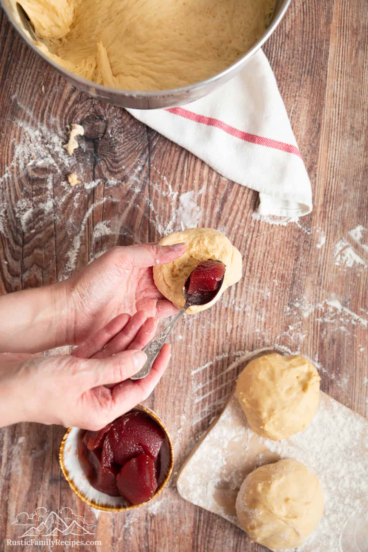A spoonful of strawberry jam being added to the center of a ball of paczki dough