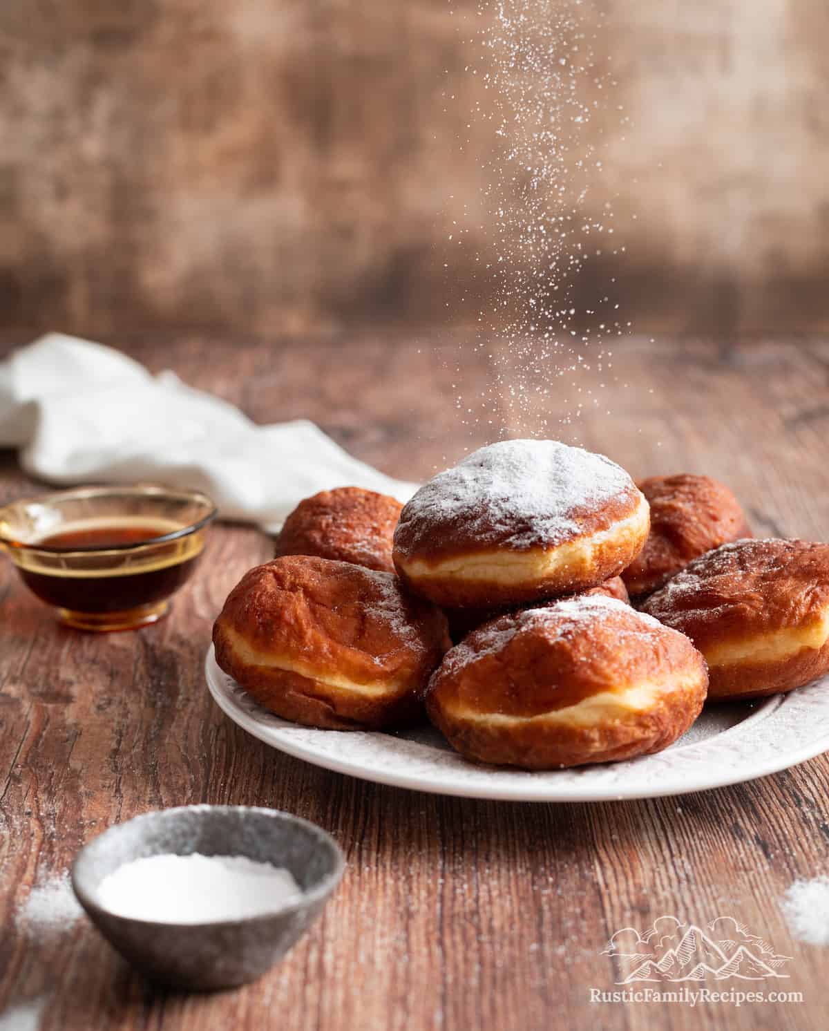 A plate full of Polish donuts topped with powdered sugar