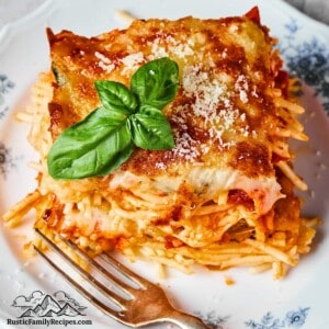 A serving of zucchini parmesan garnished with basil leaves on a white plate next to a fork.
