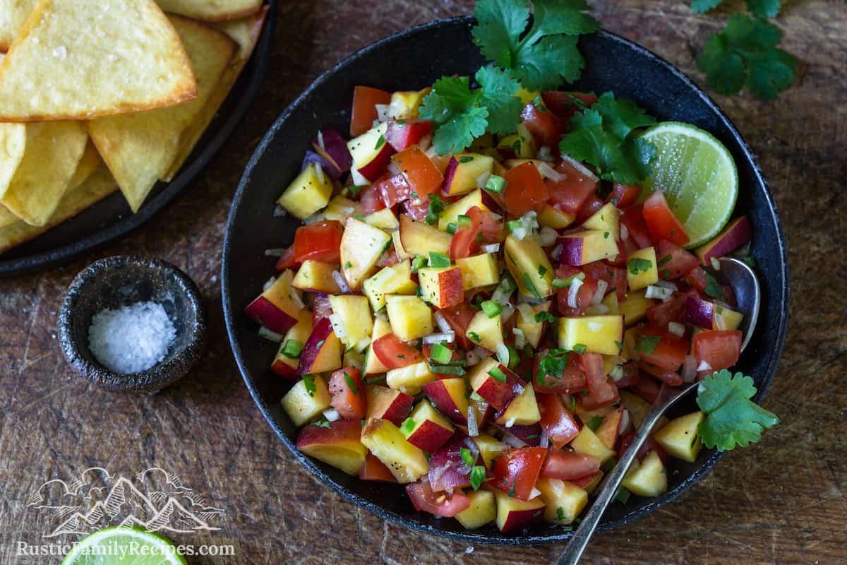 A bowl of peach salsa next to a plate of totopos