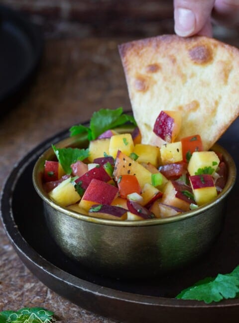 A hand dipping a tortilla chip into peach salsa