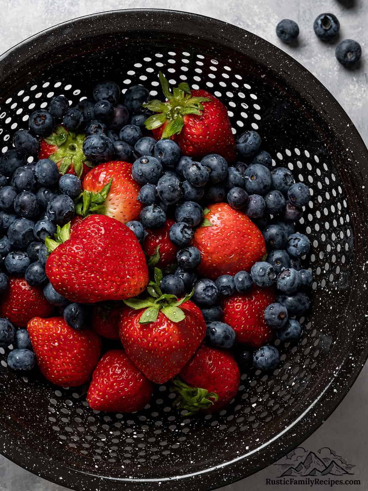 A black colander with fresh strawberries and blueberries