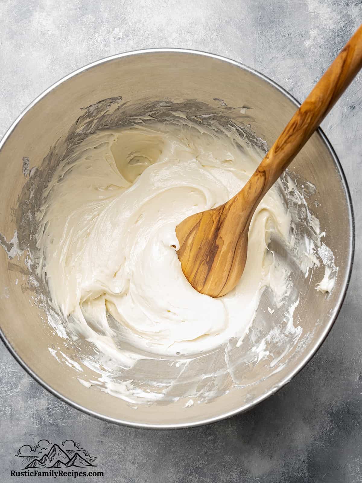 A standing mixer bowl with meringue being made and a wooden spoon
