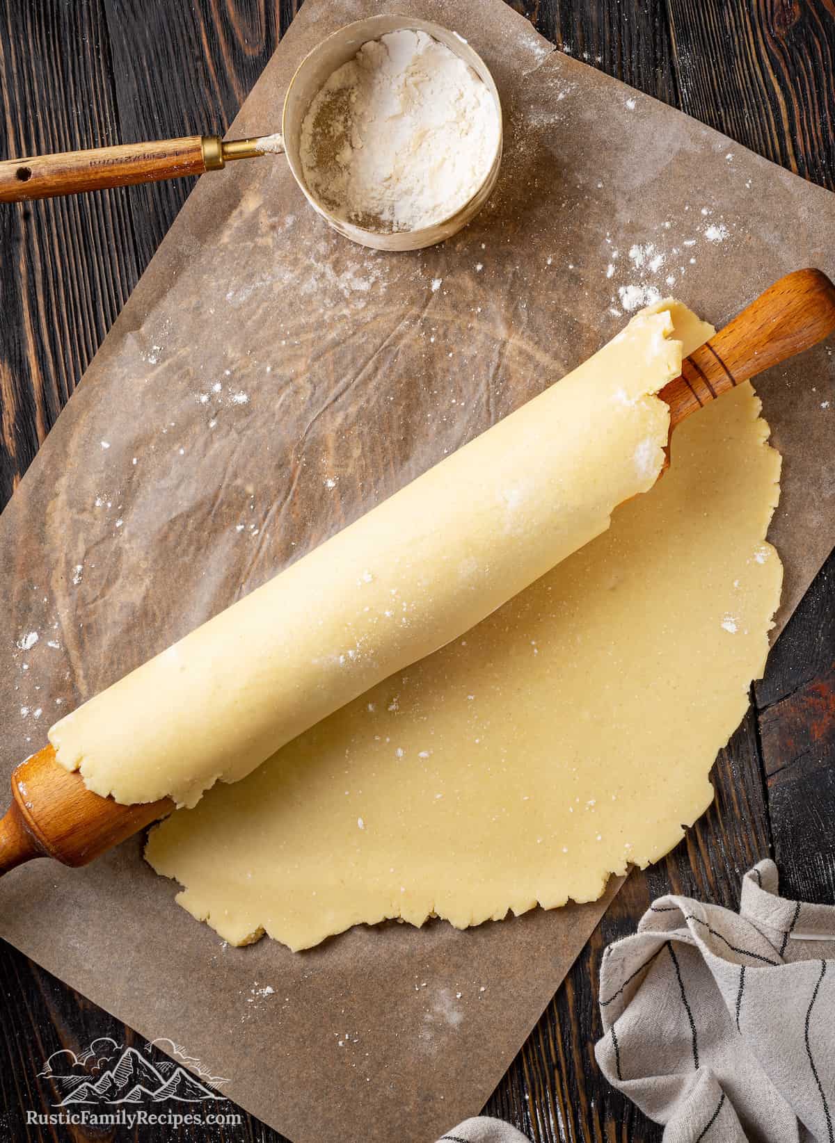 Pie crust dough wrapped around a wooden rolling pin on a floured surface.