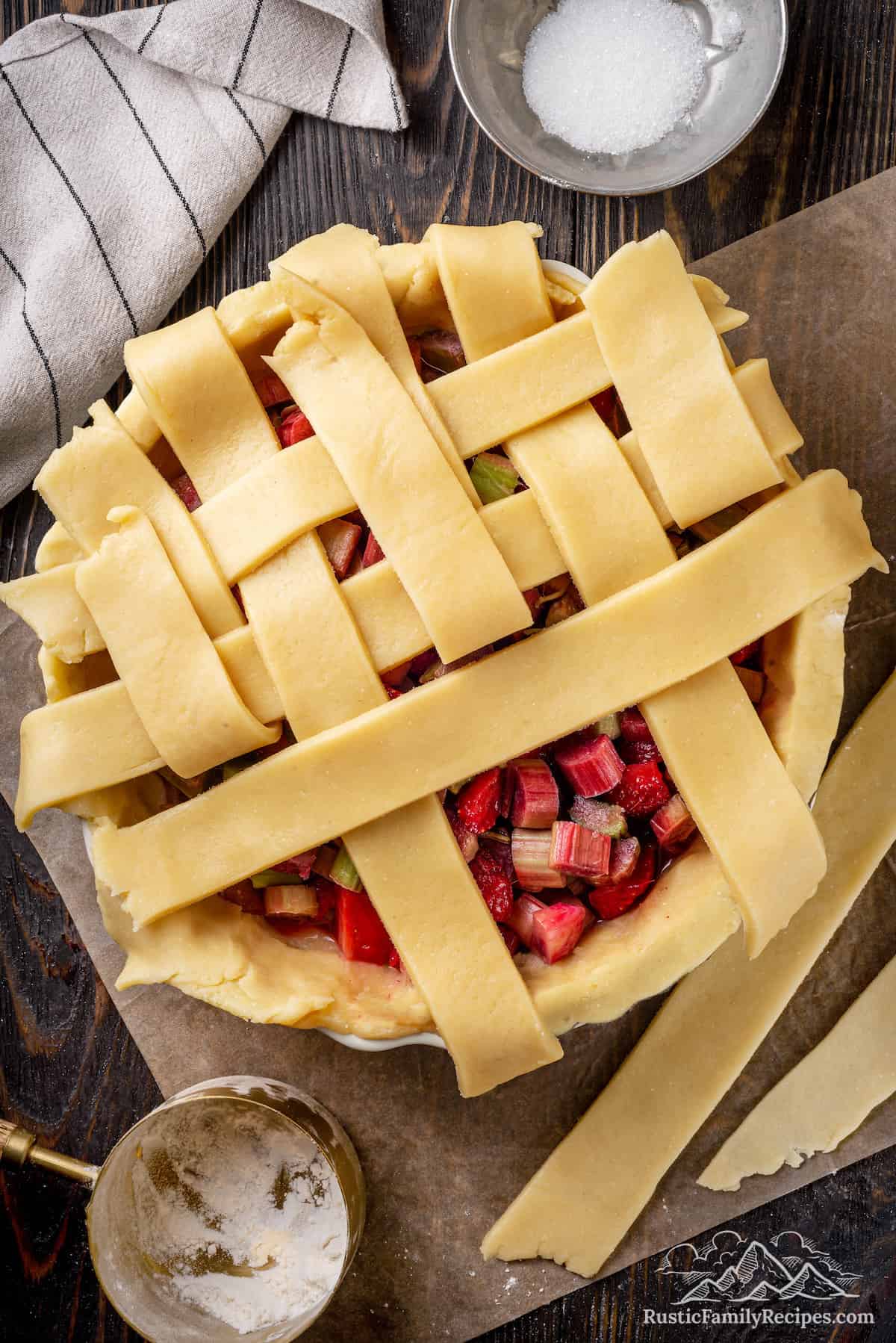 Top view of the lattice topping being assembled over a strawberry rhubarb pie.