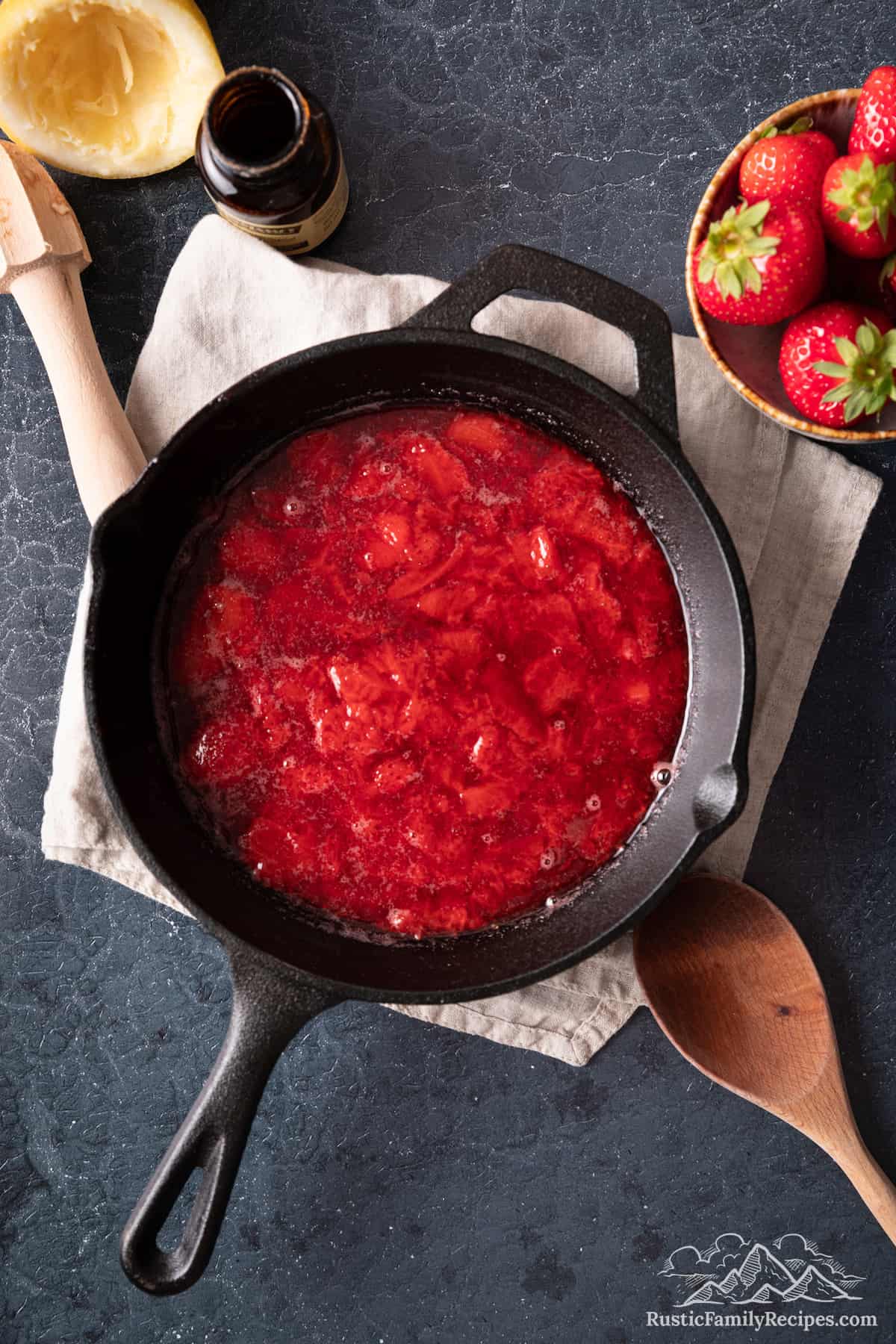 Fresh strawberry sauce in a skillet next to a bowl of berries