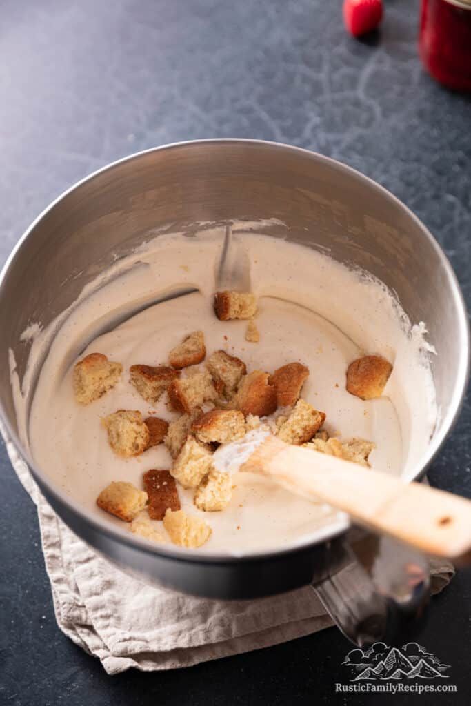 Shortcake biscuit pieces scattered over the ice cream base in a bowl, with a wooden spatula.