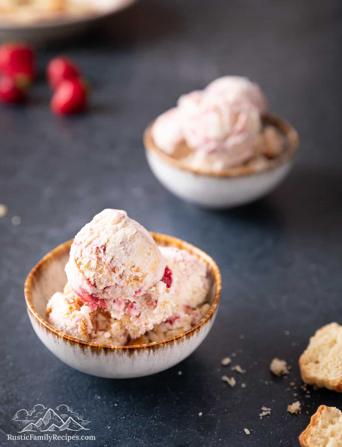 Two bowls of strawberry shortcake ice cream on a dark grey counter top.