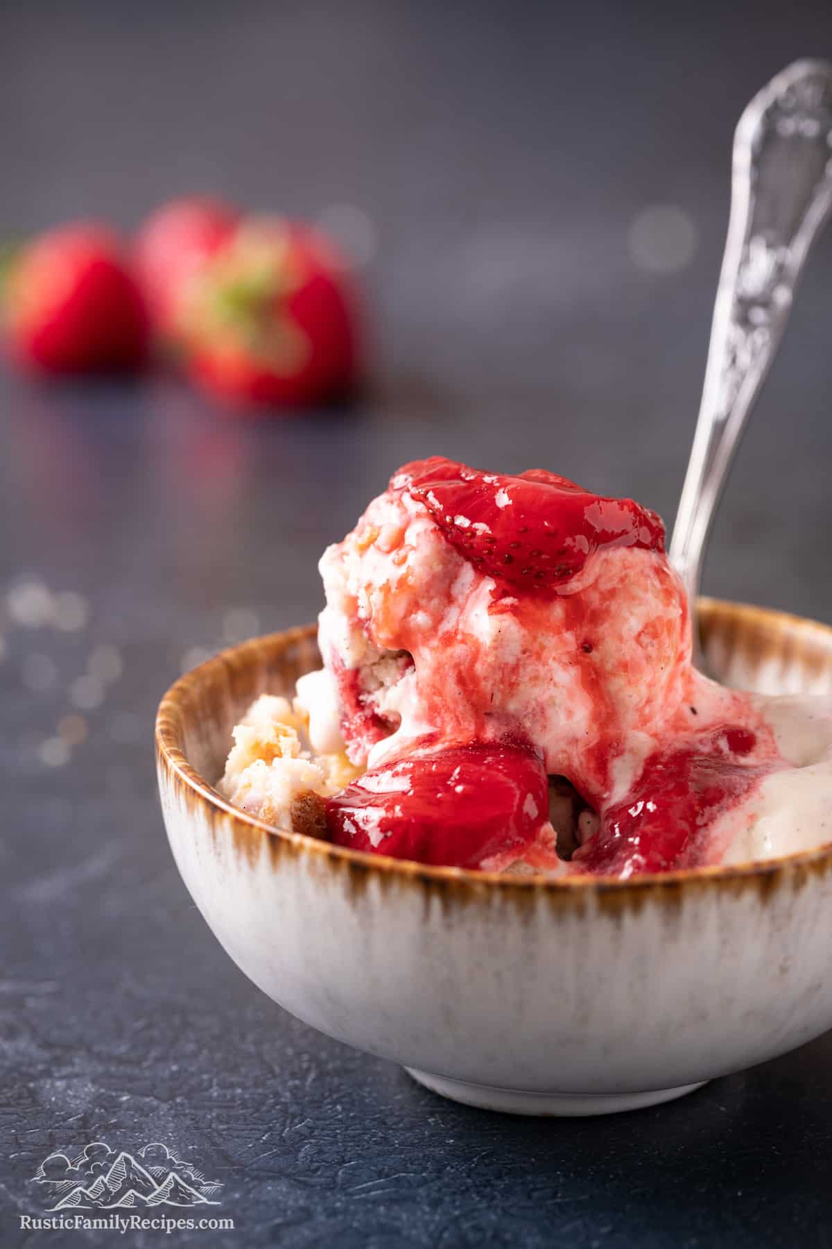 A bowl of strawberry shortcake ice cream topped with strawberry sauce with a spoon.