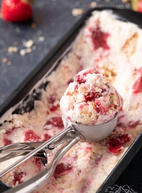 An ice cream scoops a serving of strawberry shortcake ice cream from a loaf pan.