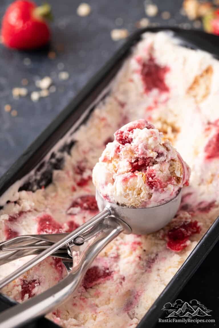An ice cream scoops a serving of strawberry shortcake ice cream from a loaf pan.