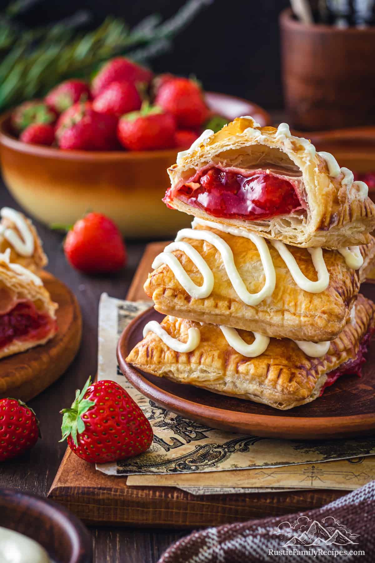 Three frosted strawberry toaster strudels stacked on top of each other on a napkin, with the top strudel cut in half to show the strawberry filling.