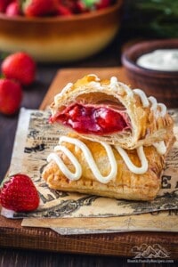 Two frosted strawberry toaster strudels stacked on top of each other on a napkin, with the top strudel cut in half to show the strawberry filling.