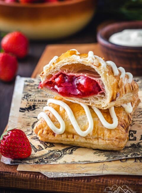 Two frosted strawberry toaster strudels stacked on top of each other on a napkin, with the top strudel cut in half to show the strawberry filling.