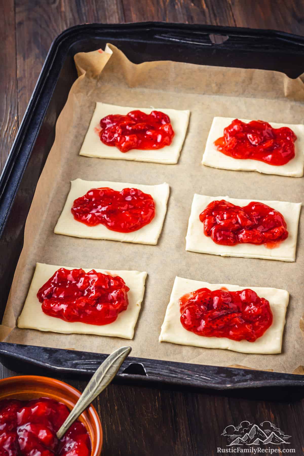 Six pastry sheets on a parchment-lined baking pan topped with strawberry filling.