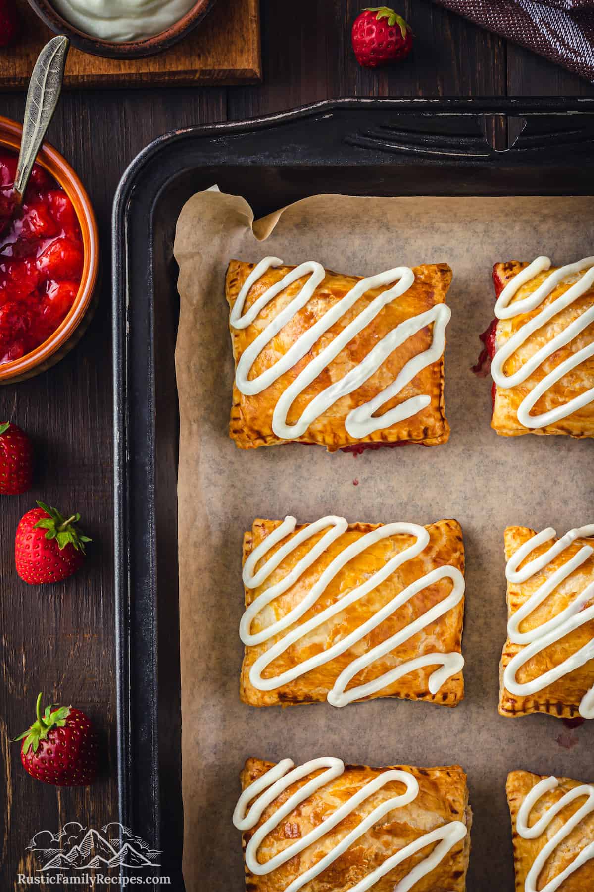 Top view of baked strawberry toaster strudels on a baking sheet topped with squiggles of cream cheese frosting.