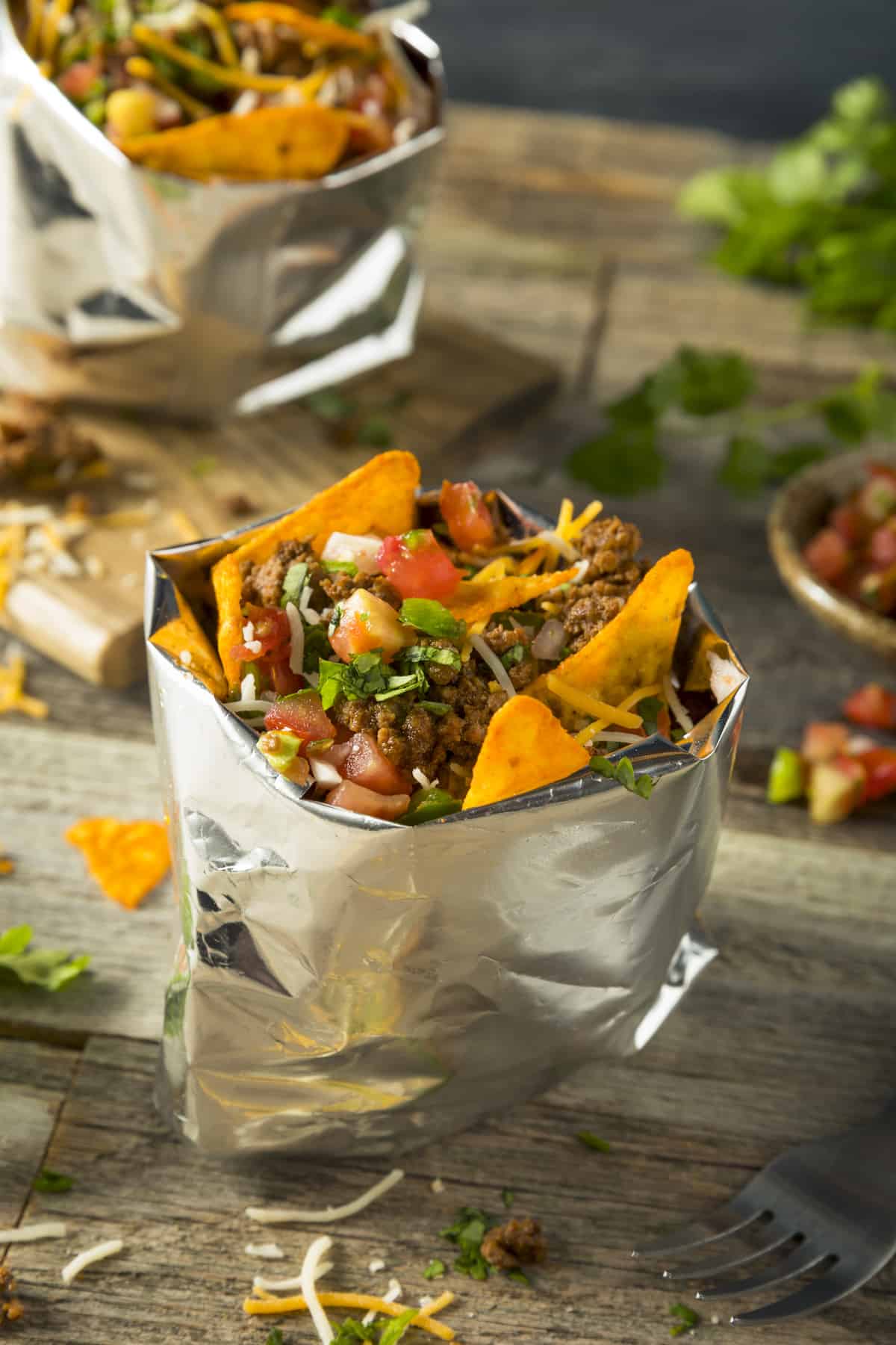 A bag with chips, taco meat, fixings and a fork