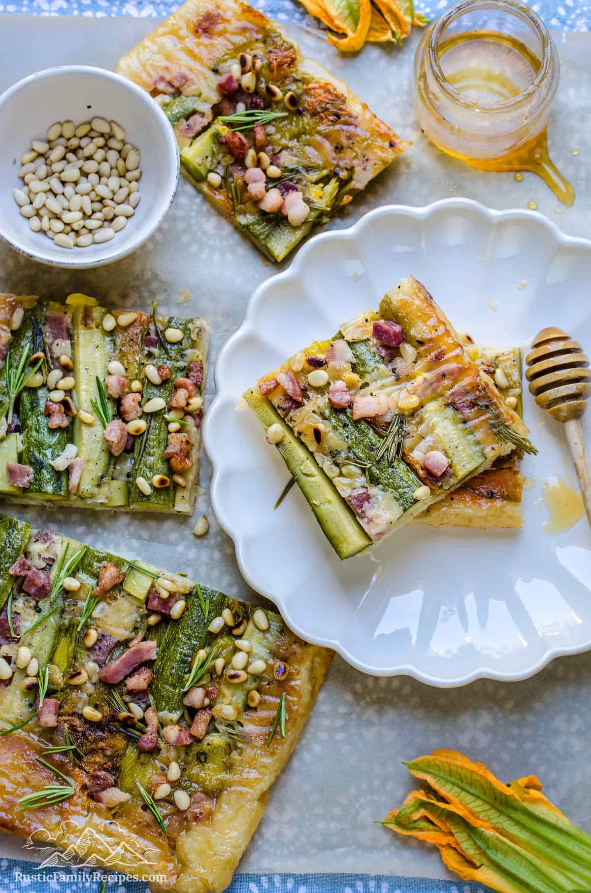 Two slices of zucchini tart stacked on a white plate, surrounded by more slices.