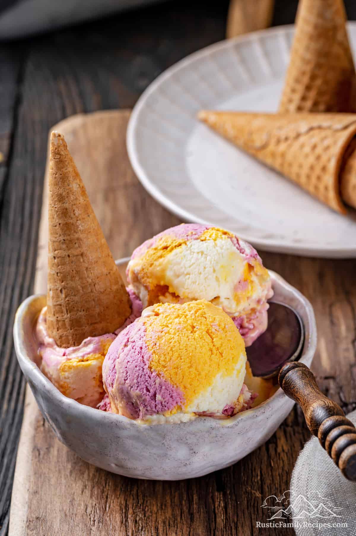 Scoops of rainbow sherbet in a bowl with a spoon, topped with a sugar cone.