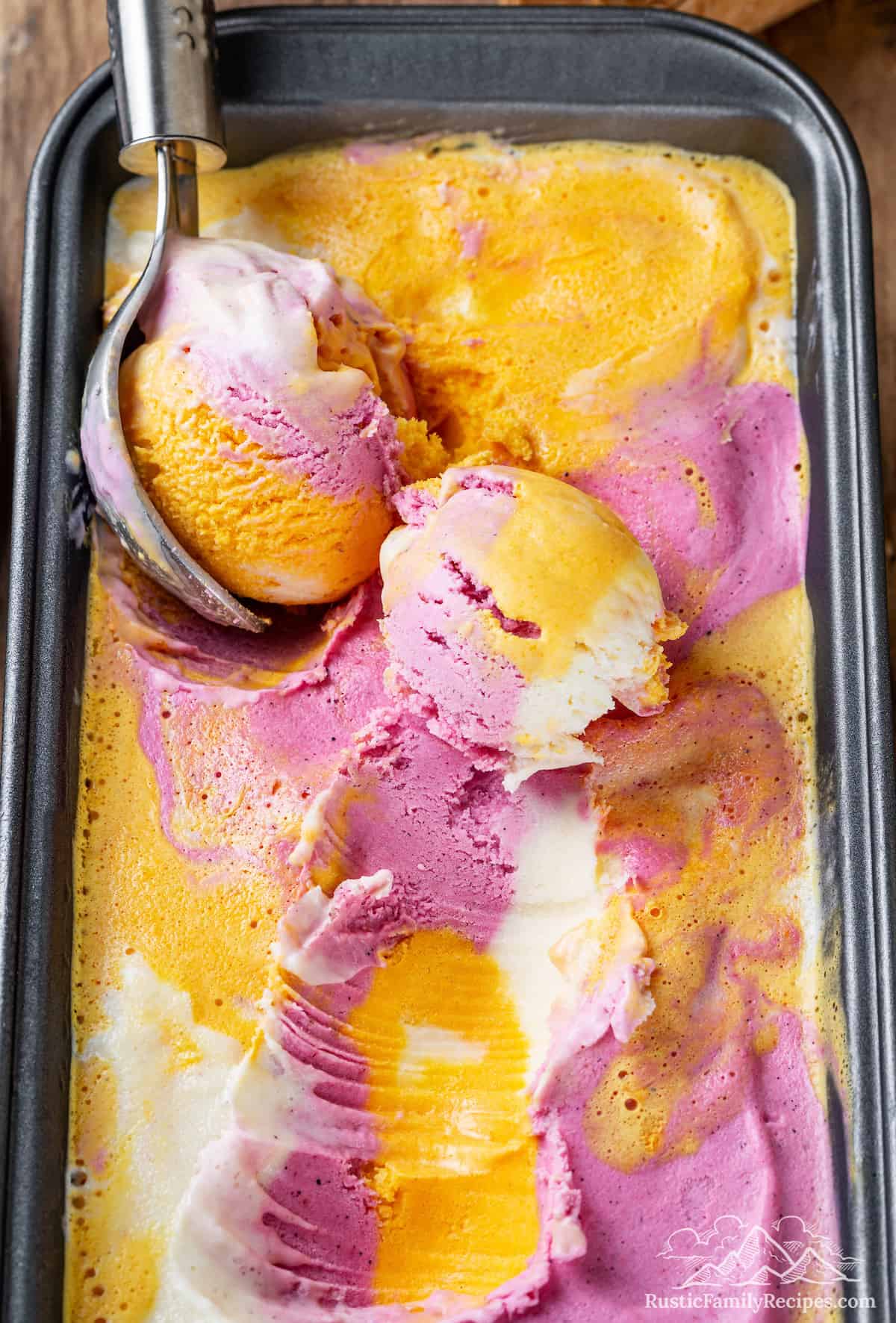 Top view of rainbow sherbet in a loaf pan, with an ice cream scoop.