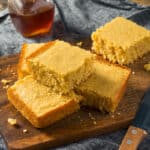 Slices of cornbread stacked on a cutting board with honey