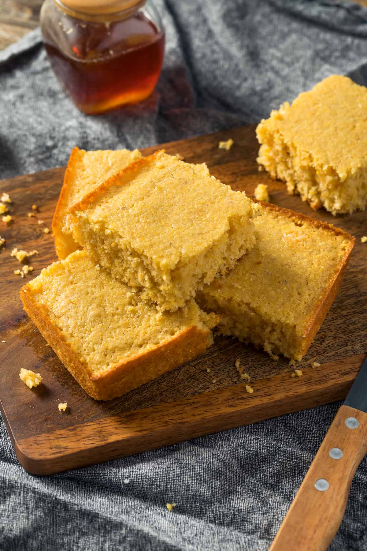 Slices of cornbread stacked on a cutting board with honey