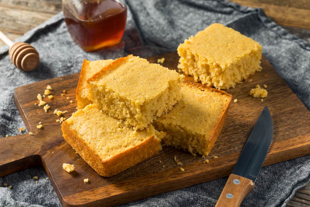 Slices of cornbread stacked on a cutting board with honey