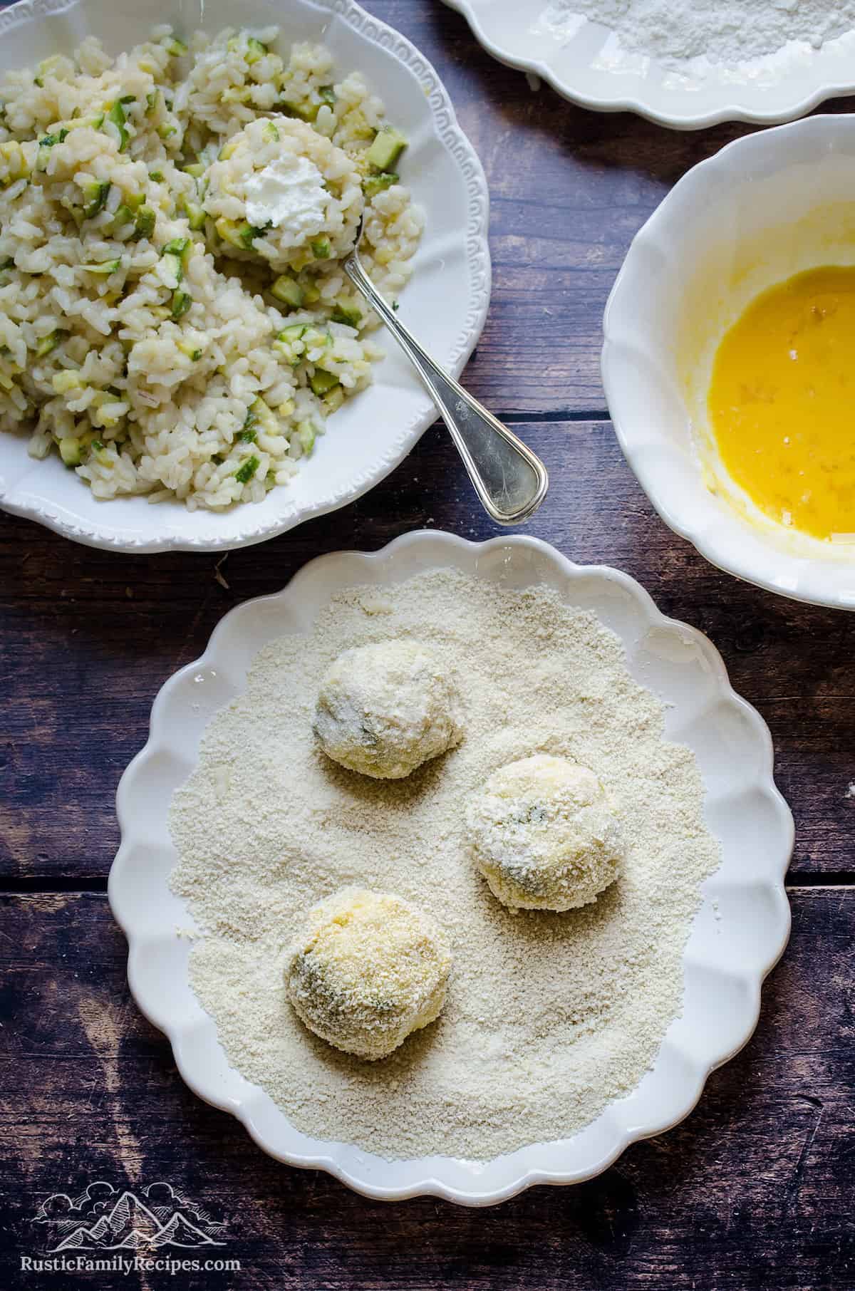 Three risotto balls rolled in a dish full of breadcrumbs.