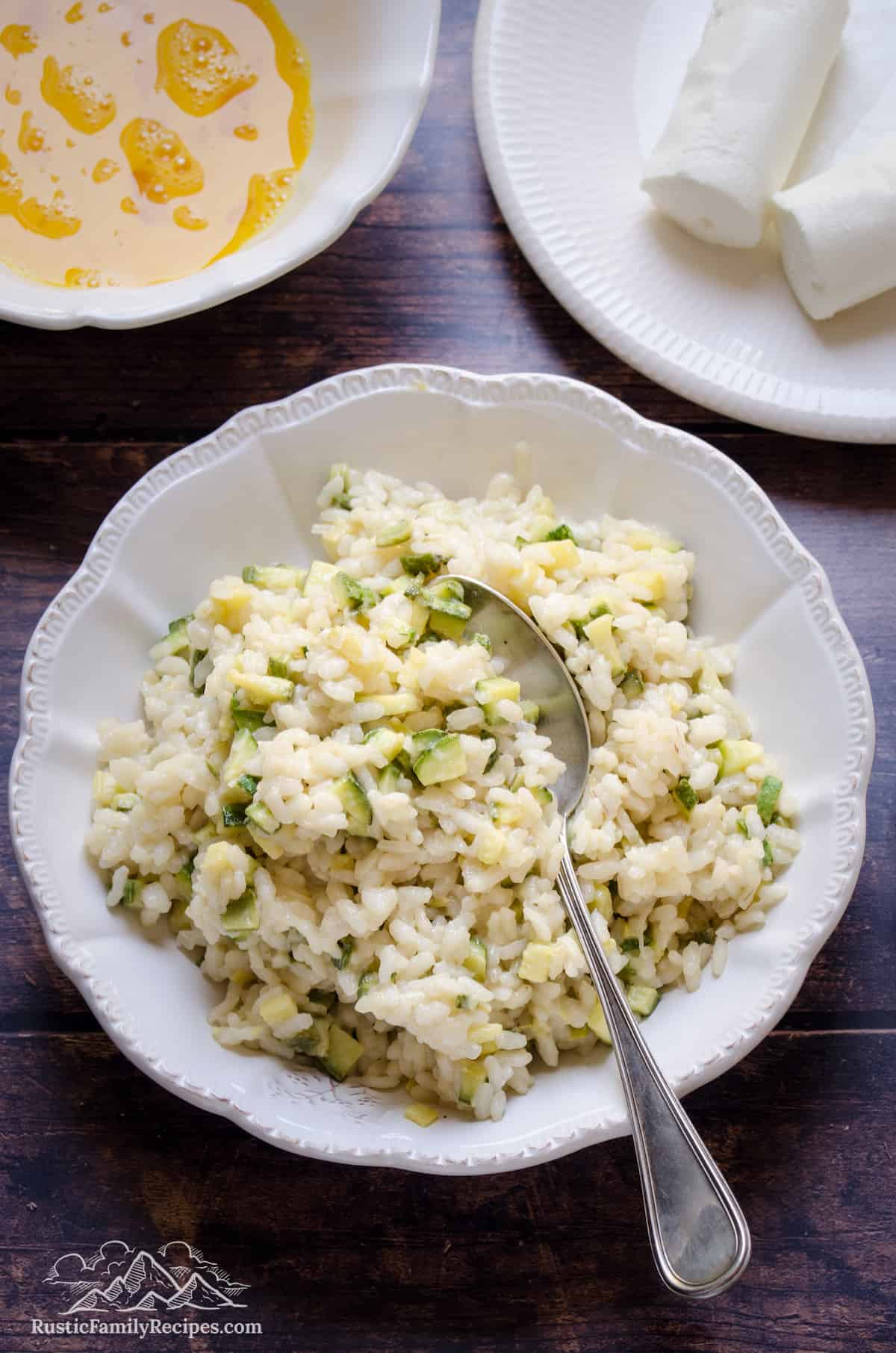 Cooked zucchini risotto rice in a white bowl with a spoon.