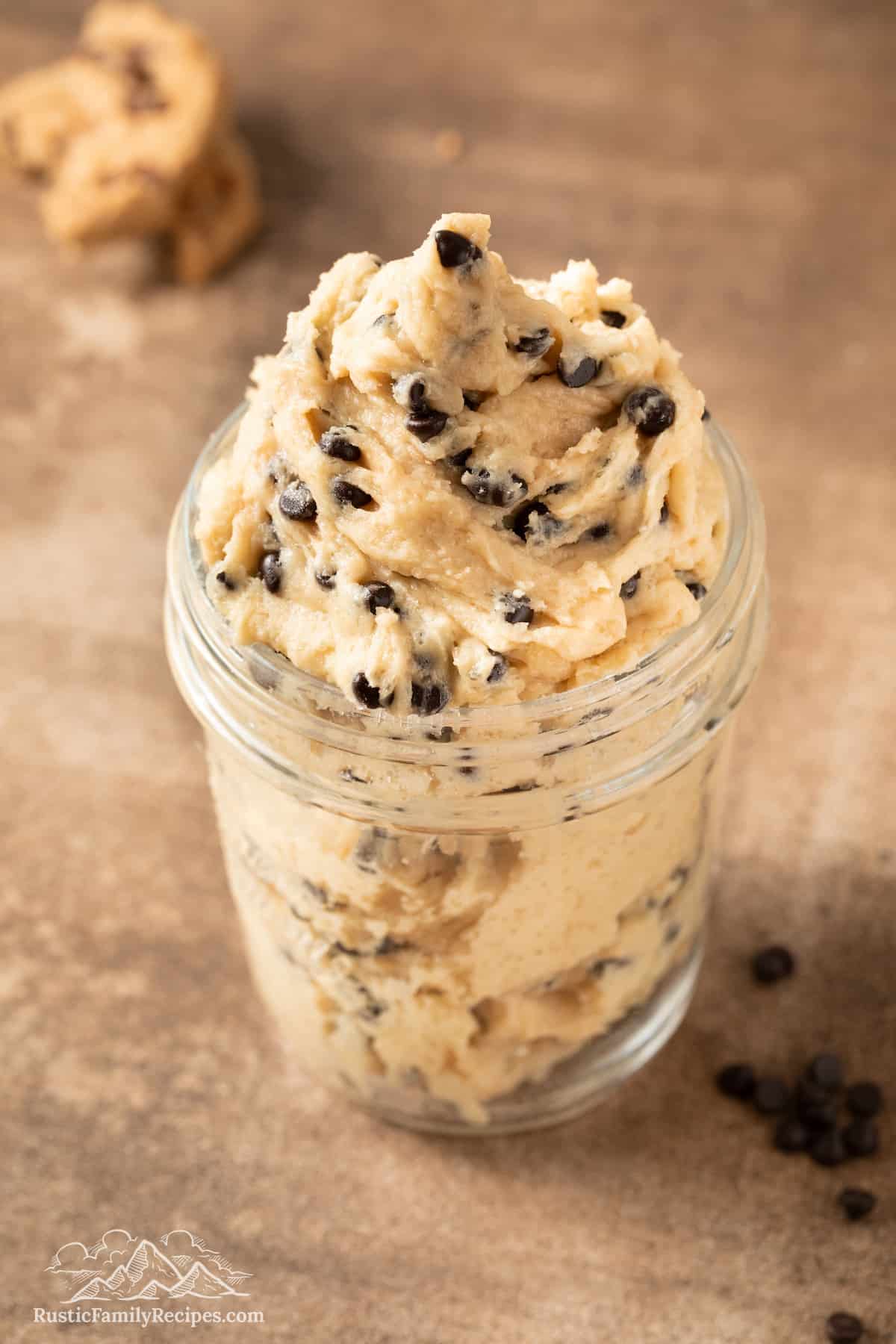 A mason jar with edible chocolate chip cookie dough and spoonful bedside it