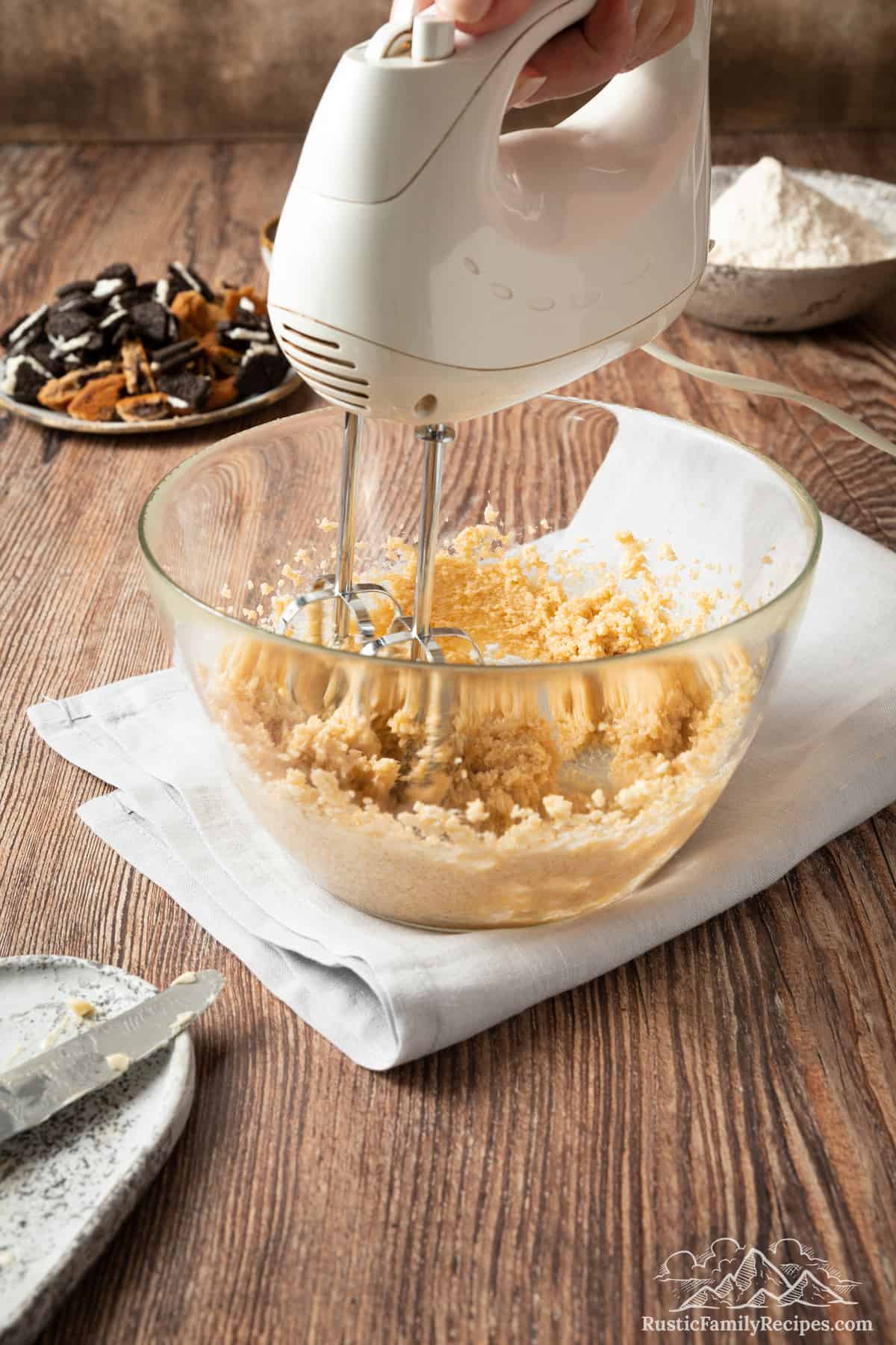 Cookie dough ingredients are beaten together in a glass mixing bowl with a stand mixer.